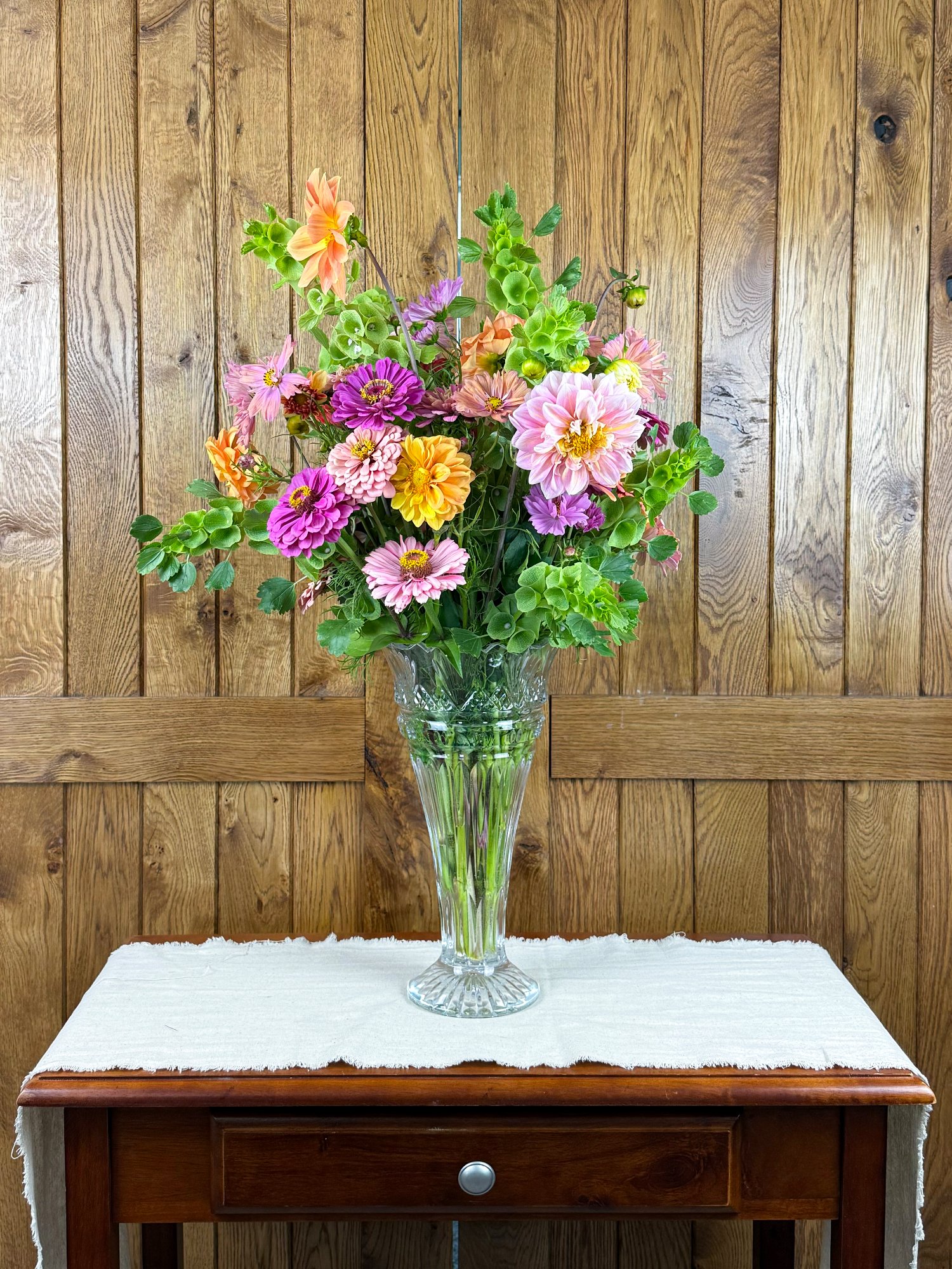 A pink, orange, and green gathering containing dahlias, zinnias, and bells of Ireland.